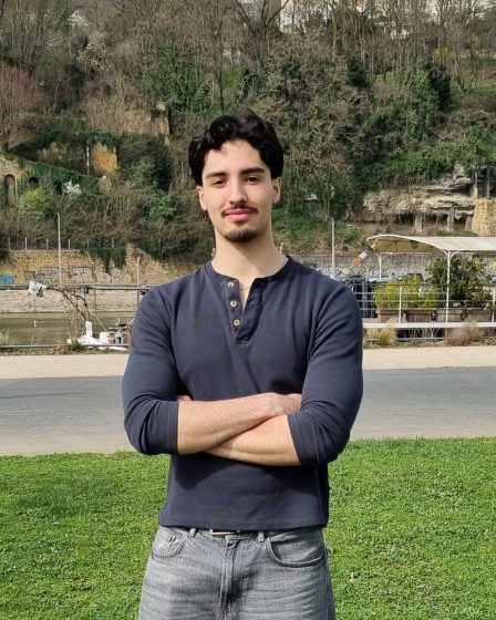 Portrait de Fares Ben Mohamed, étudiant en droit, posant en extérieur les bras croisés.