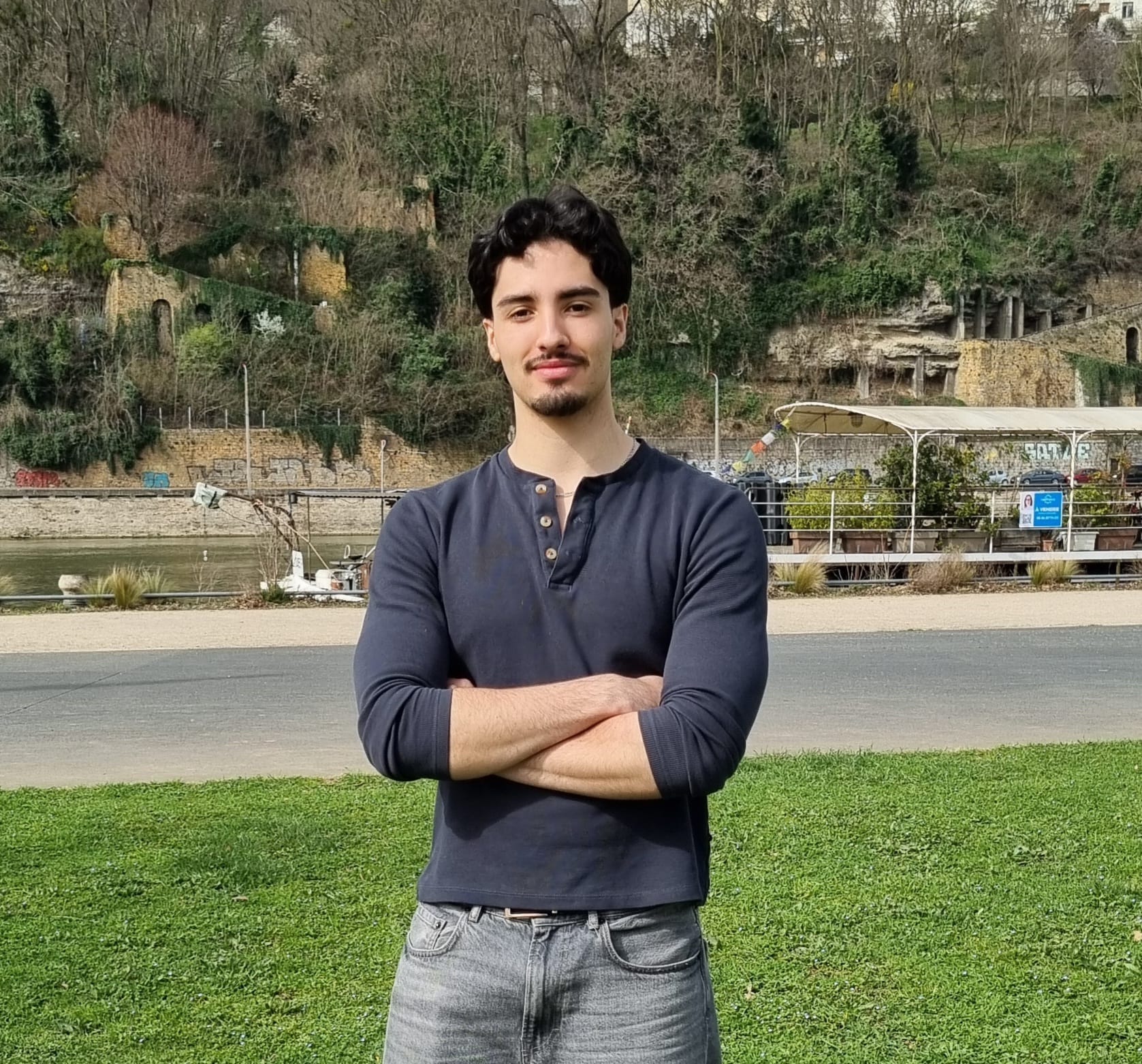 Portrait de Fares Ben Mohamed, étudiant en droit, posant en extérieur les bras croisés.