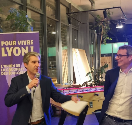 François Ruffin (à gauche) s'exprimant au microphone lors d'un événement, avec Boris Tavernier (à droite) adossé à un poteau en l'écoutant.