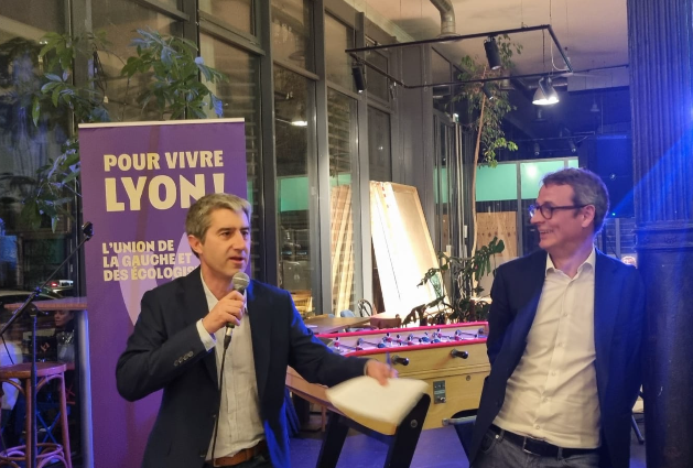 François Ruffin (à gauche) s'exprimant au microphone lors d'un événement, avec Boris Tavernier (à droite) adossé à un poteau en l'écoutant.